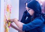 A photograph of two women sorting sticky notes on a wall.